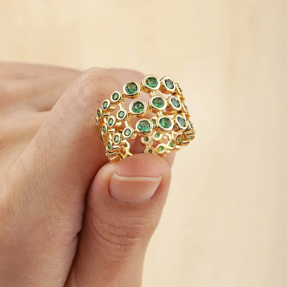 Wide gold plated copper ring with a full band of sparkling green cubic zirconia stones on a hand.