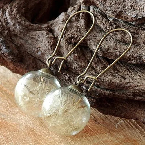 Close-up of a transparent 16mm glass ball earring with a dandelion seed inside, on a silver French hook.
