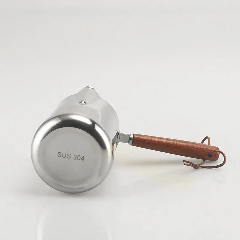 Stainless steel barista milk jug with wooden handle and internal measurement scale for latte art.
