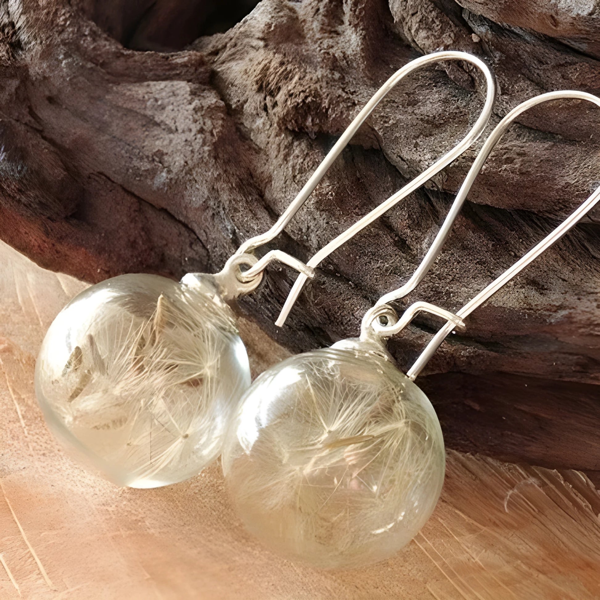 Close-up of a transparent 16mm glass ball earring with a dandelion seed inside, on a silver French hook.