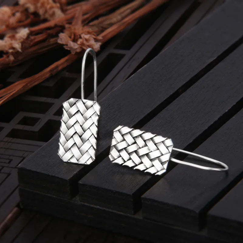 Close-up of a pair of silver geometric stud earrings with a woven diamond plaid pattern on a white background.