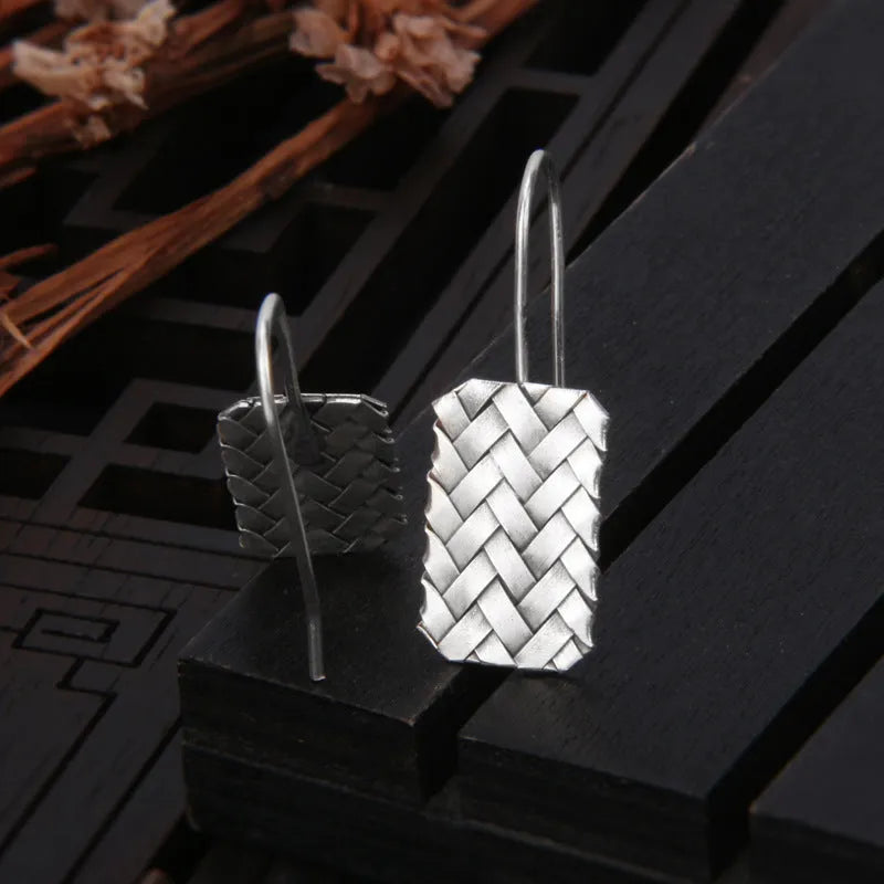 A pair of silver geometric stud earrings with a woven diamond plaid texture on a plain background.