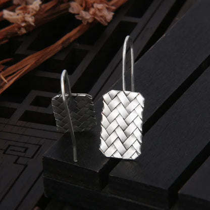 A pair of silver geometric stud earrings with a woven diamond plaid texture on a plain background.