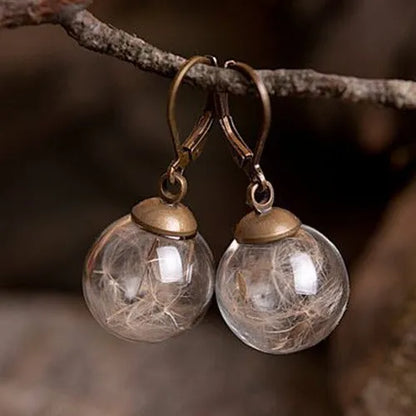 Close-up of a transparent 16mm glass ball earring with a dandelion seed inside, on a silver French hook.