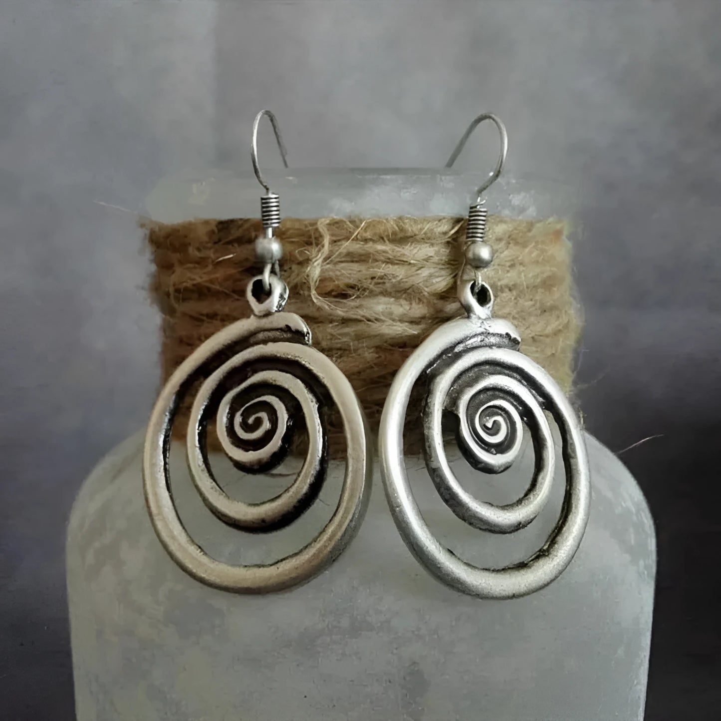 A pair of silver spiral geometric earrings with a distressed texture, shown from the front.