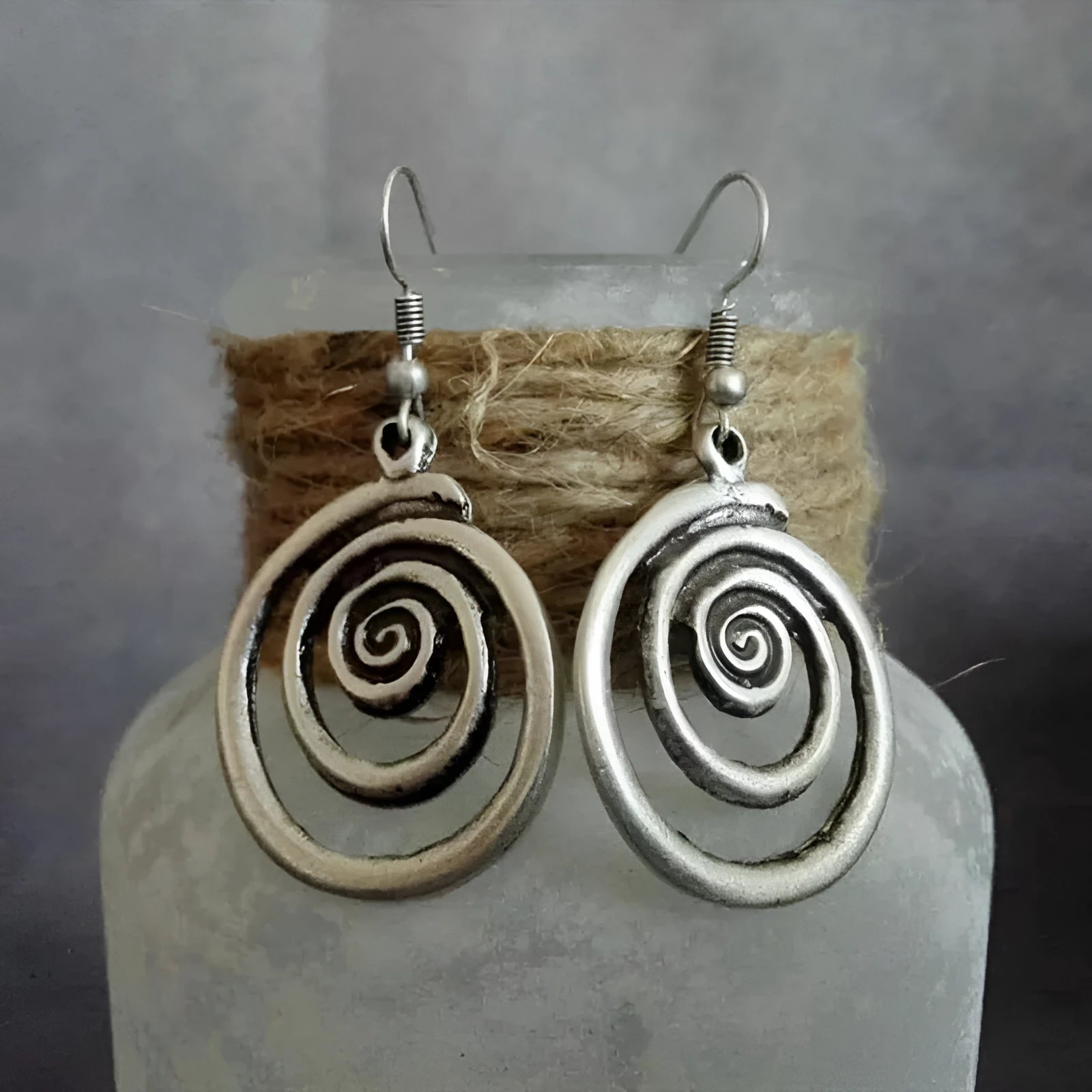 A pair of silver spiral geometric earrings with a distressed texture, shown from the front.