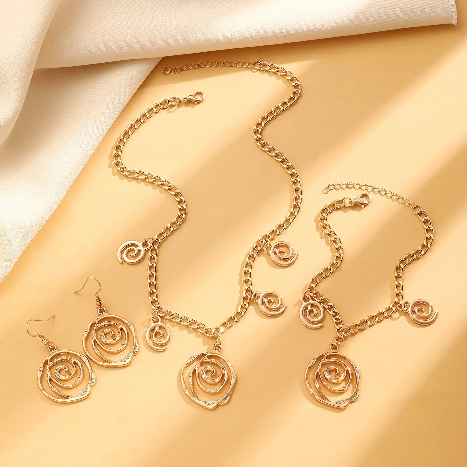 Gold spiral donut alloy jewellery set showing necklace, bracelet, and ear hooks on a plain background.