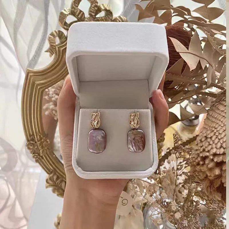 A pair of square stud earrings with a natural freshwater pearl in a geometric alloy setting.