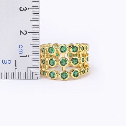 Wide gold plated copper ring with a full band of sparkling green cubic zirconia stones on a hand.