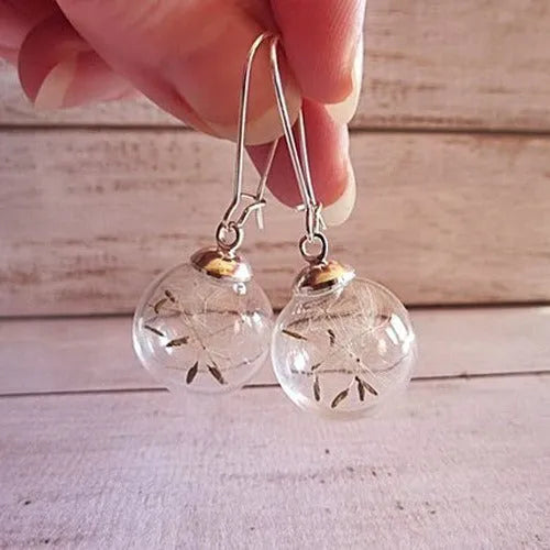 Close-up of a transparent 16mm glass ball earring with a dandelion seed inside, on a silver French hook.