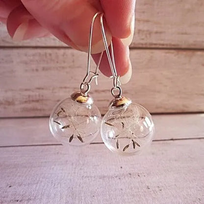 Close-up of a transparent 16mm glass ball earring with a dandelion seed inside, on a silver French hook.