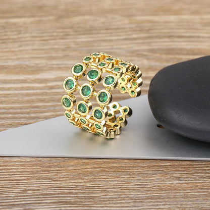 Wide gold plated copper ring with a full band of sparkling green cubic zirconia stones on a hand.