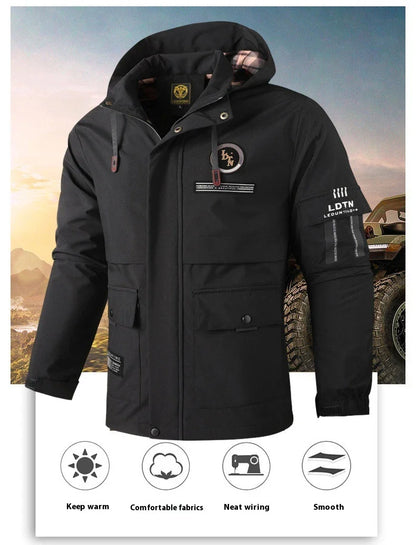 A man wearing a black, waterproof and hooded outdoor jacket, standing in front of a scenic mountain landscape.