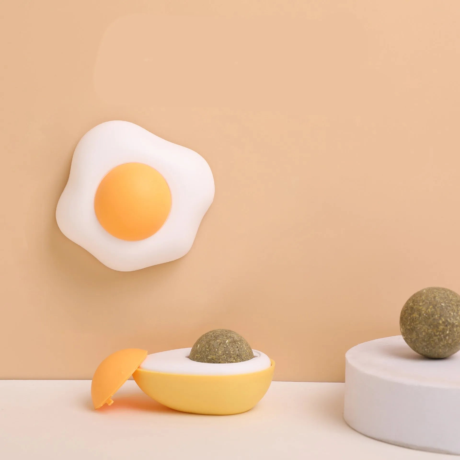 Interactive plush catnip ball toy shaped like a fried egg, stuck to a wall with a cat batting at it.
