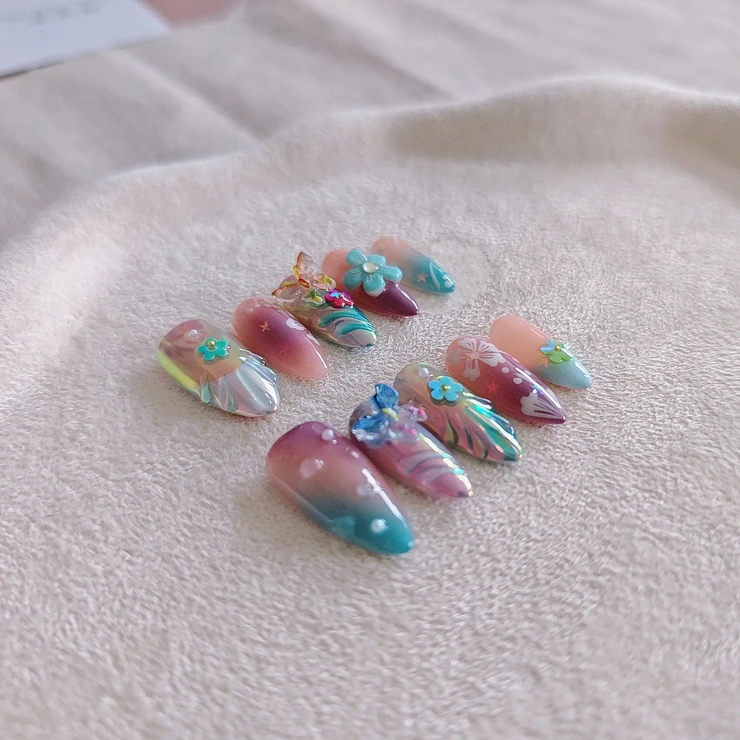 Handmade small 3D nail art sculptures showing embossed butterflies and flowers in almond shapes on a manicure.