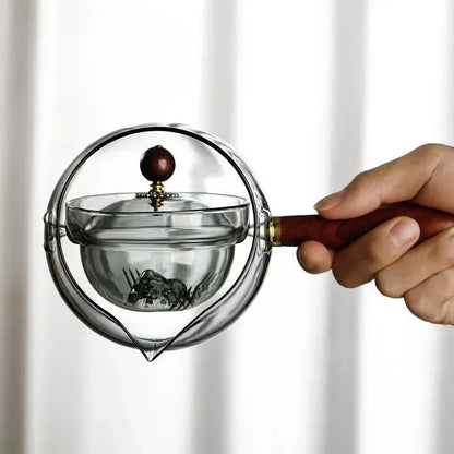Glass teapot with wooden handle showing transparent borosilicate construction and removable infuser