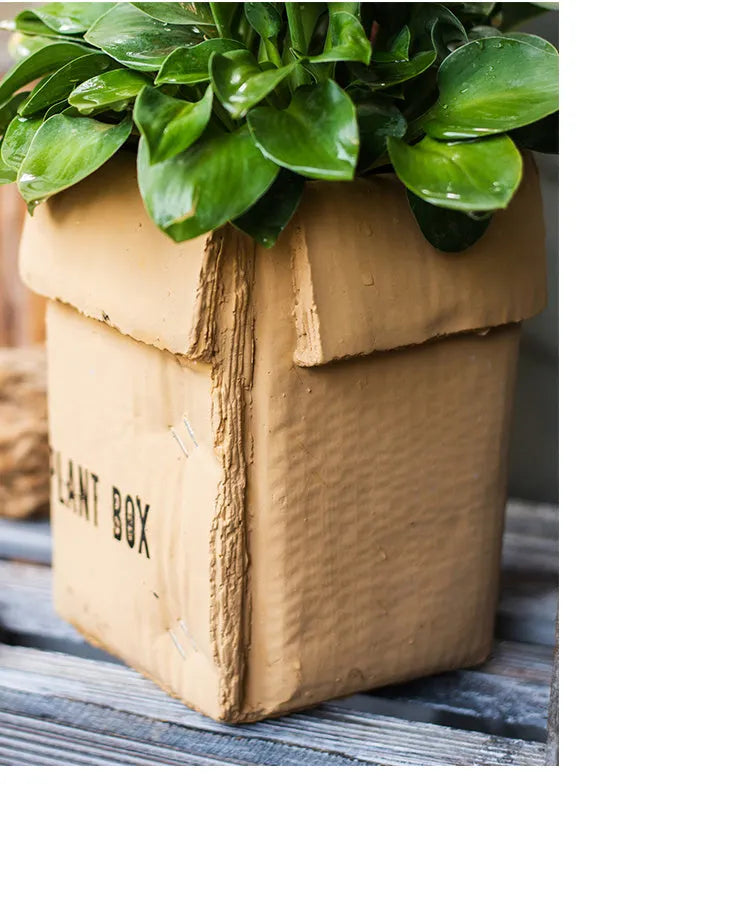 Square cement planter with matte finish and drainage holes, next to a small green plant.