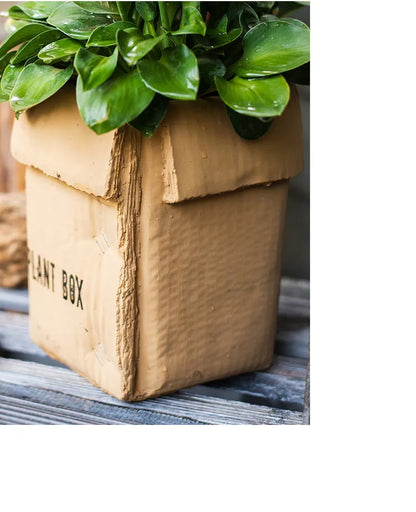 Square cement planter with matte finish and drainage holes, next to a small green plant.