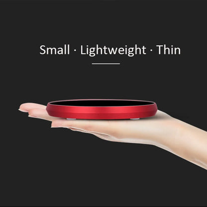 Black USB heating coaster on a desk next to a coffee mug, showing touch controls and coloured indicator light.