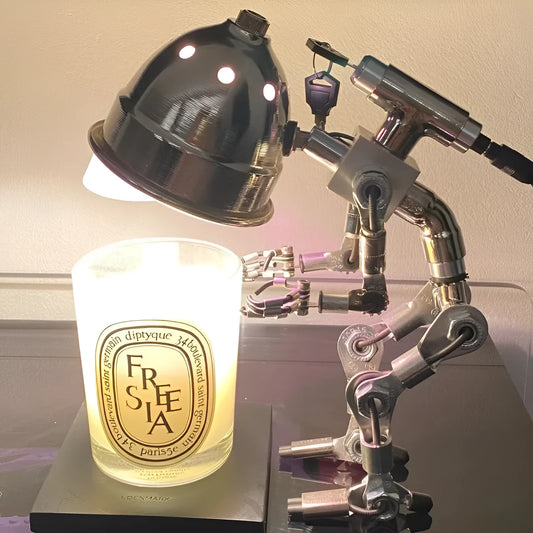 Copper robot-shaped desk lamp with custom graphic on a wooden desk next to a book.