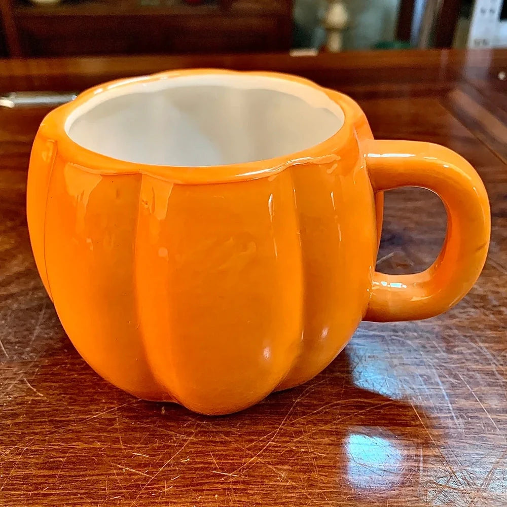 Orange ceramic Halloween pumpkin mug with cartoon face and included spoon on autumn table