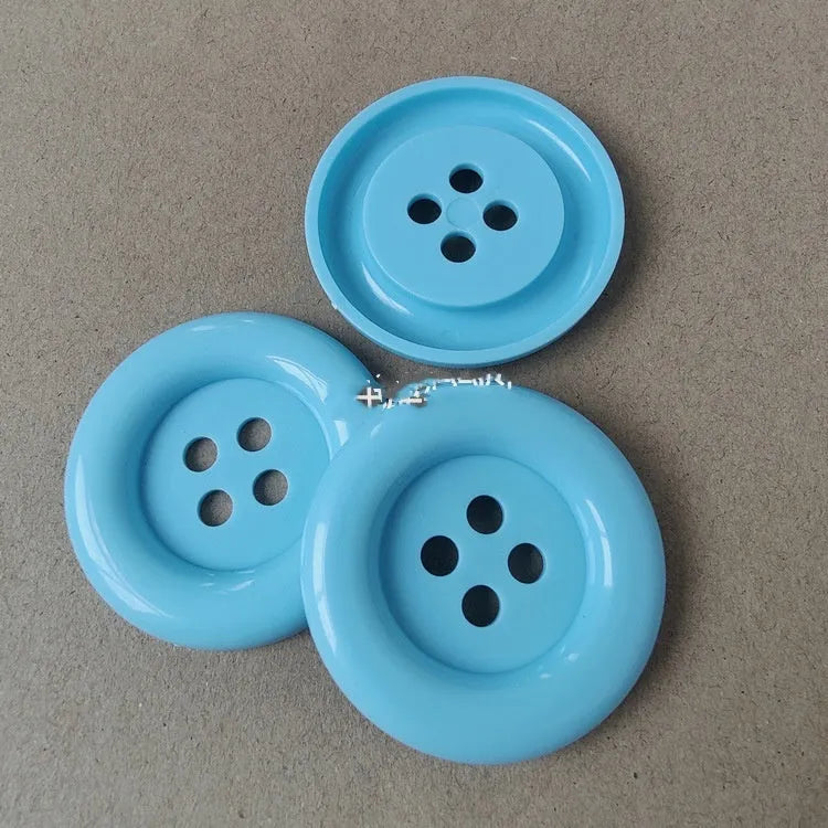 Assorted oversized round plastic buttons in various colours showing four-hole sew-through design.