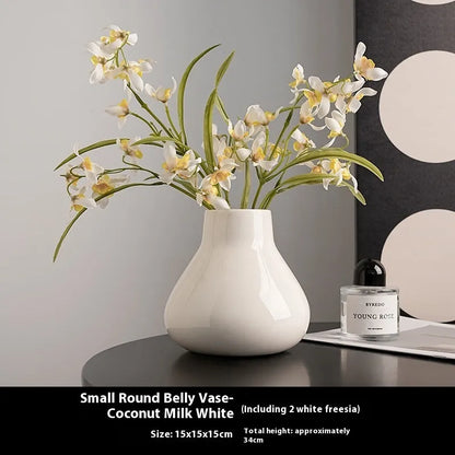 Black ceramic vase with round belly design and two white artificial orchid stems on wooden table