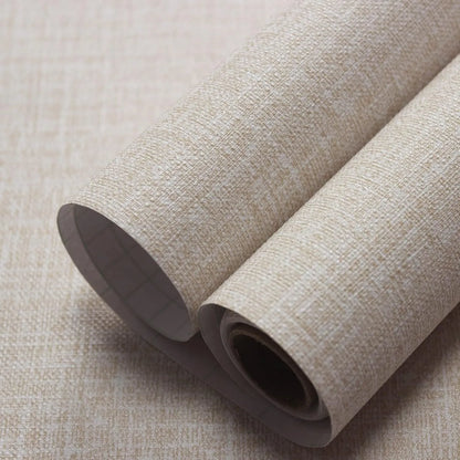 Roll of beige linen self-adhesive wallpaper with textured finish next to a sample applied to a clean white wall.