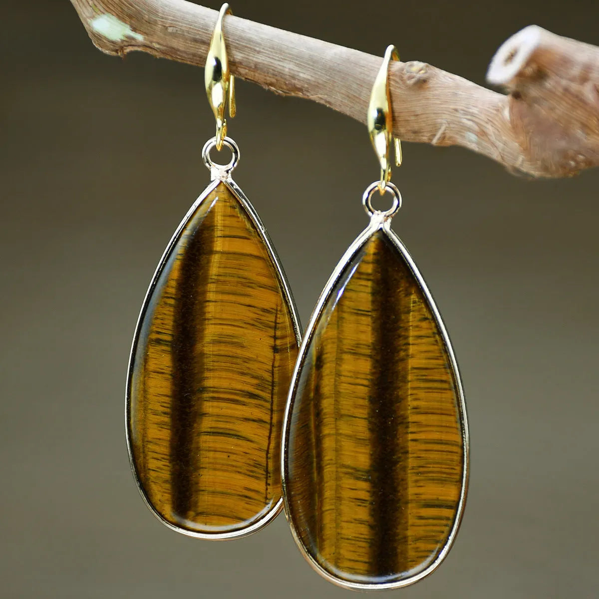 Close-up of long, polished tigereye stone drop earrings with a fishhook clasp on a neutral background.