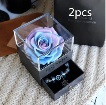 Blue and pink eternal flower gift box with roses and carnations on a table.