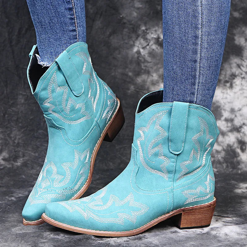 Women's brown embroidered cowboy boots with a low wedge heel and pointed toe on a wooden floor.