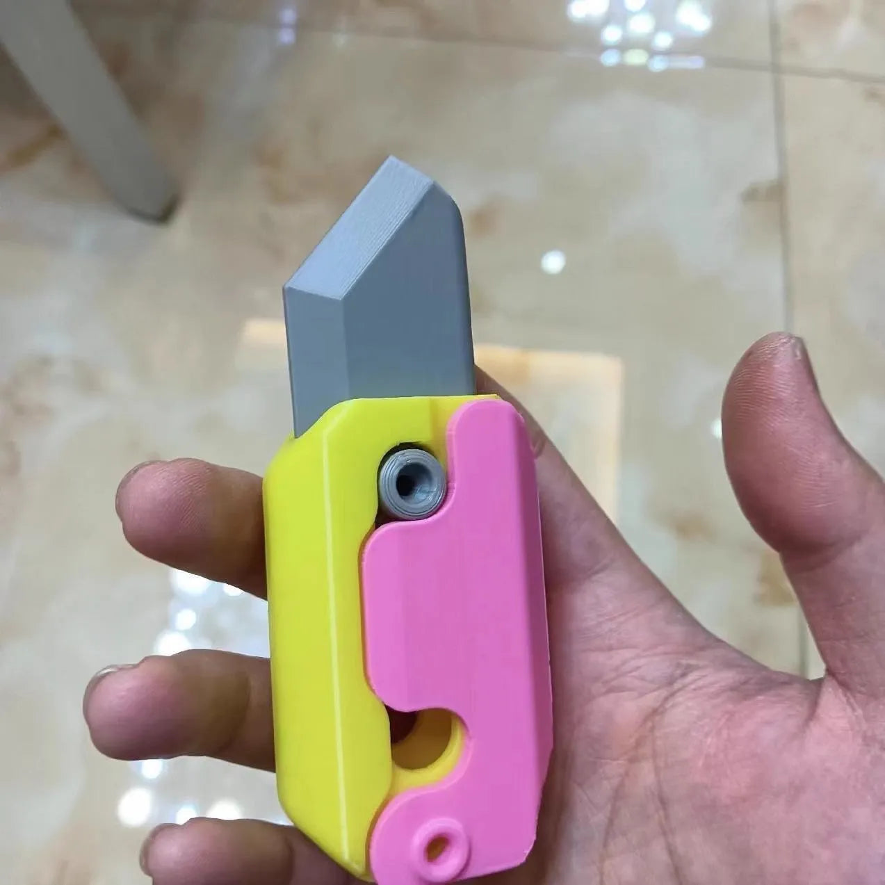 Small orange and green 3D printed plastic carrot knife fidget toy with blade extended.
