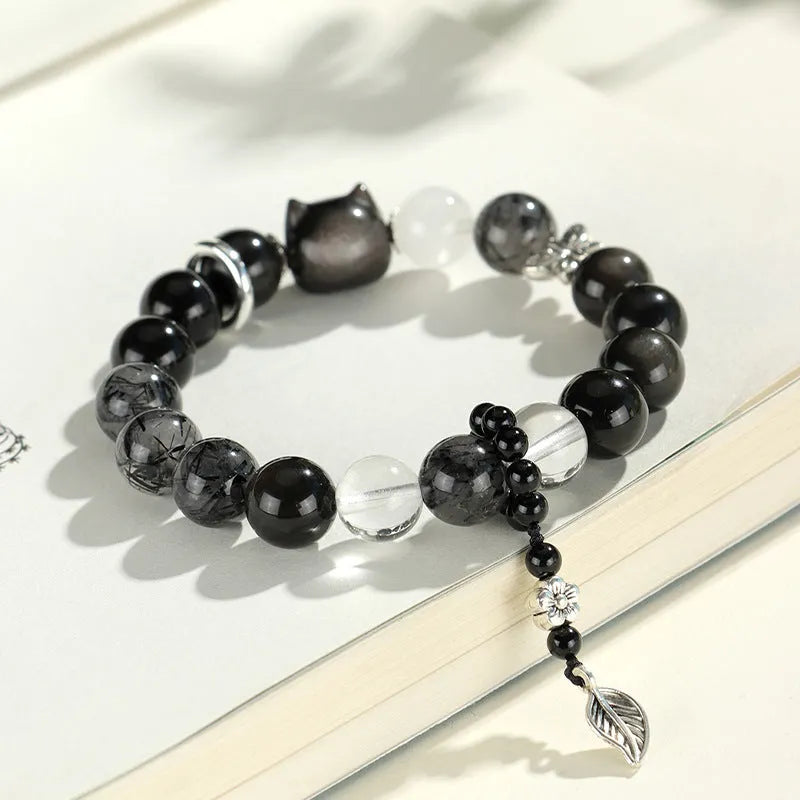 Silver stone crystal bracelet with diamond-shaped fox, cat head, and planet charms on white background.