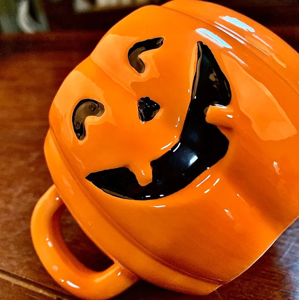 Orange ceramic Halloween pumpkin mug with cartoon face and included spoon on autumn table