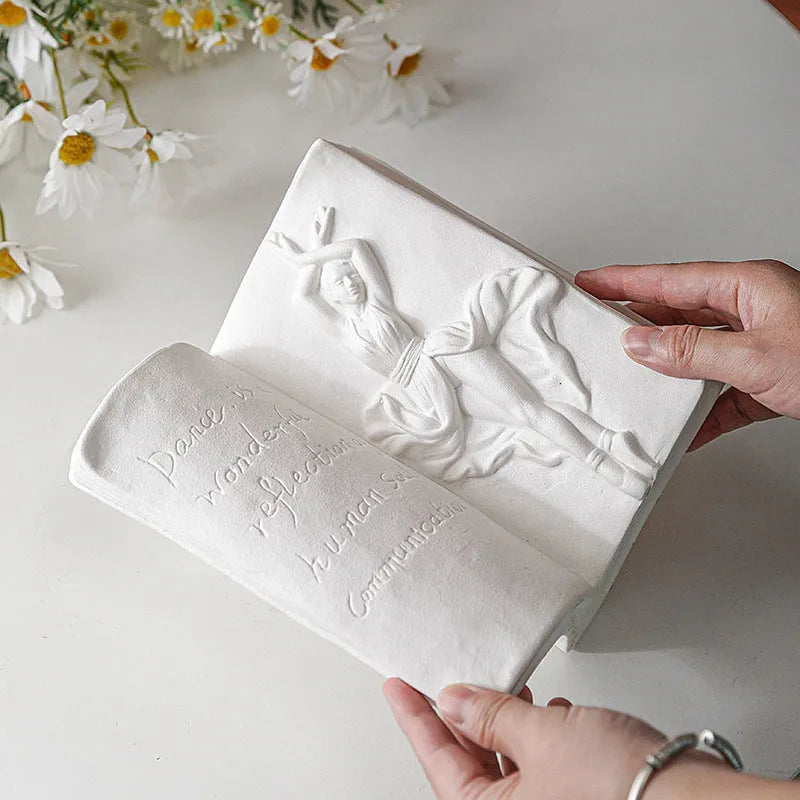 White ceramic book stand holding an open book at an angle, with a wire page holder in use.