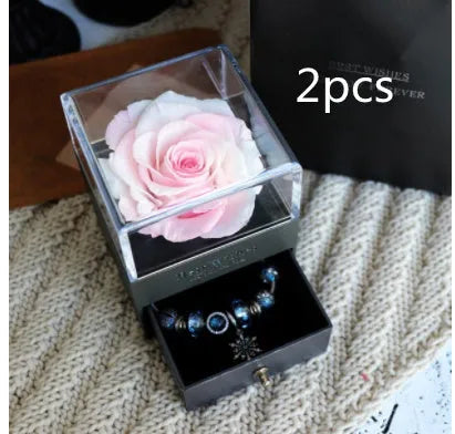 Blue and pink eternal flower gift box with roses and carnations on a table.