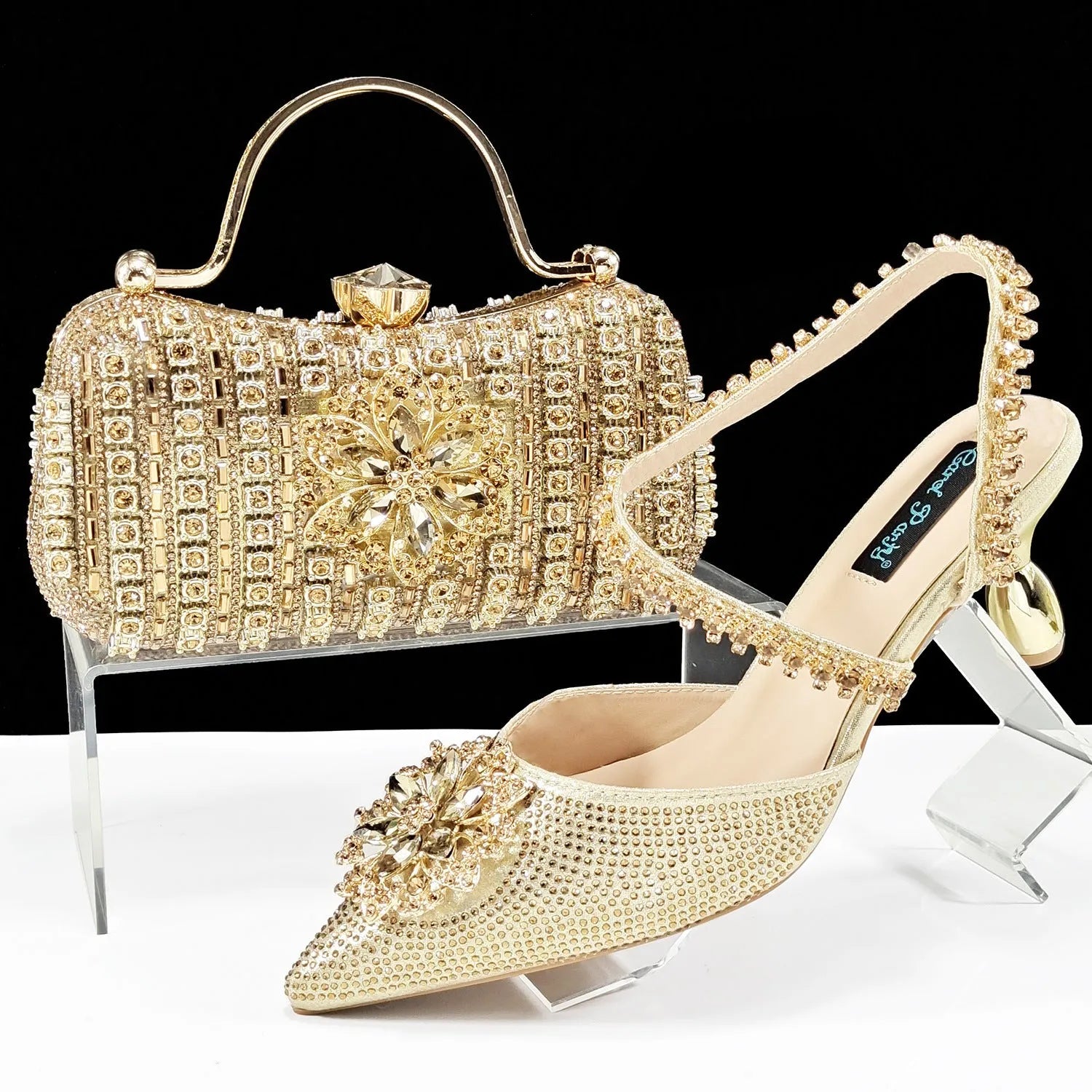 Women's black high-heel ankle strap shoes with floral rhinestone buckle and matching clutch bag on a neutral background