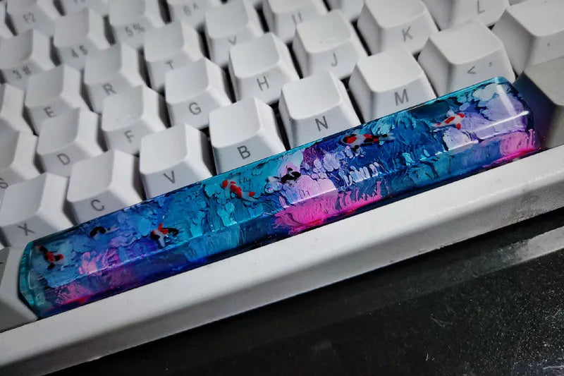 Close-up of a custom resin keycap featuring a detailed blue and orange koi fish scene, designed for Cherry MX mechanical keyboards.