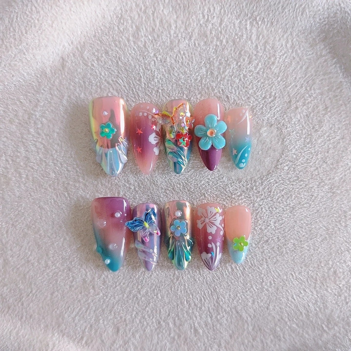 Handmade 3D sculpted butterfly and embossed flower nail art decorations in four sizes on a manicure.