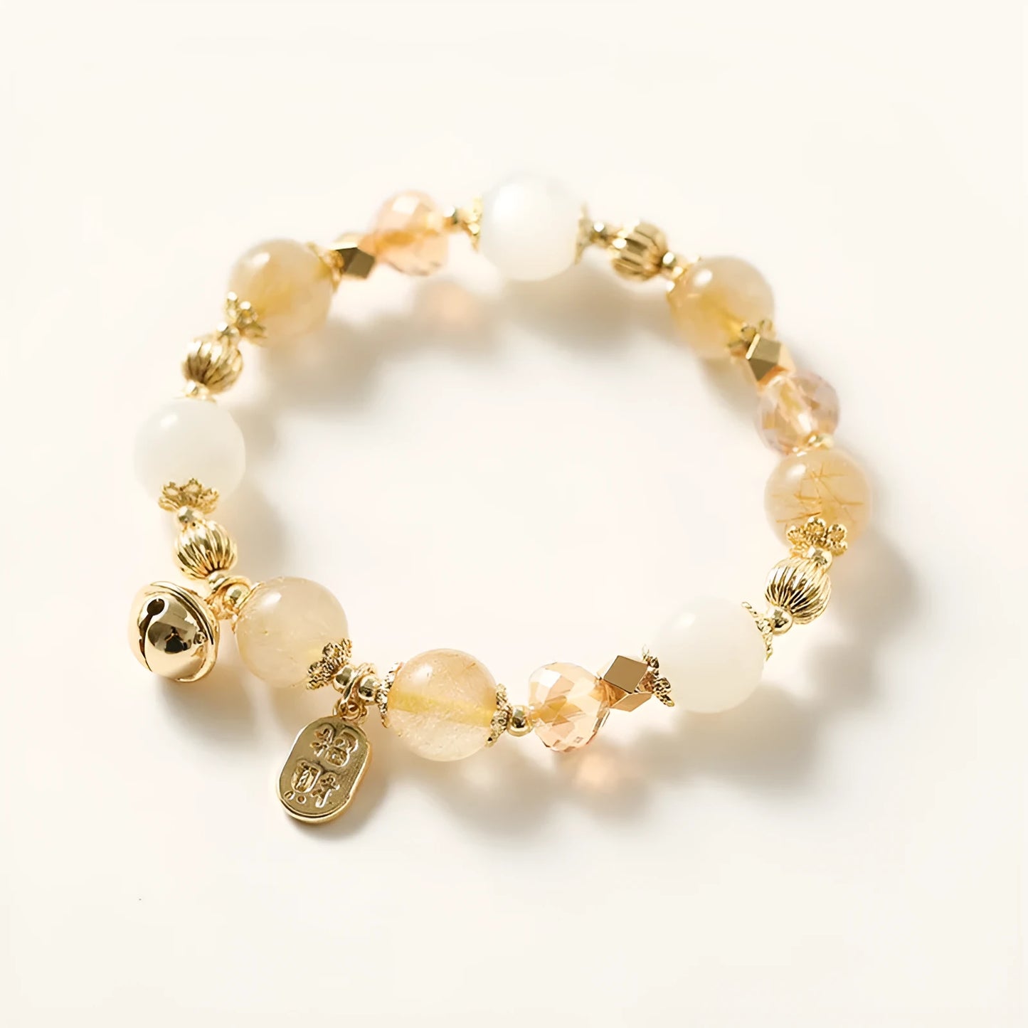 Gold-coloured rutilated quartz bracelet with a ringing bell charm on an adjustable band.