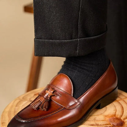 Men's black genuine leather tassel loafers with a rubber sole, shown from a side angle.