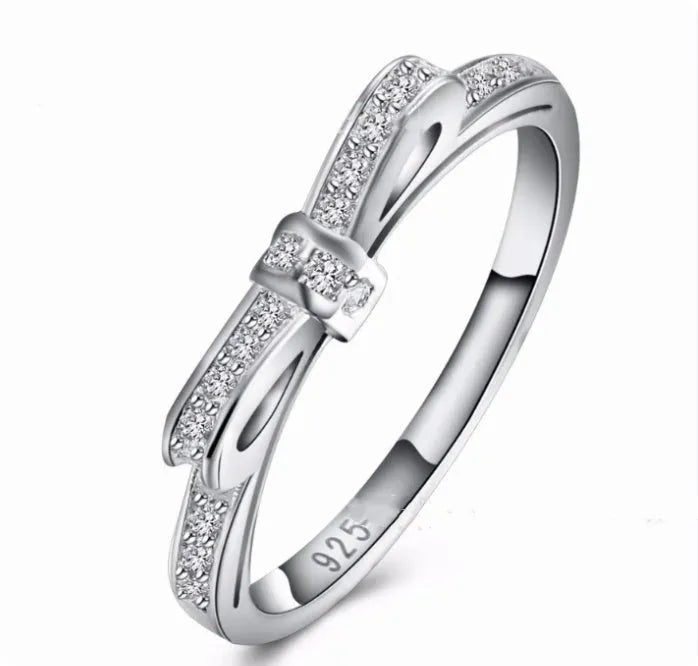Silver bow-shaped ring with zircon crystal accents on finger, showing electroplated finish and detailed bow design