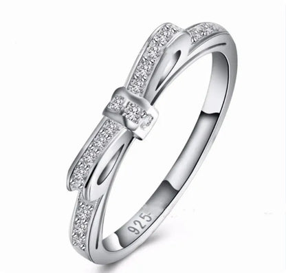 Silver bow-shaped ring with zircon crystal accents on finger, showing electroplated finish and detailed bow design