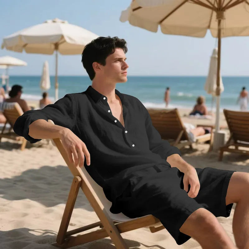 A man wearing a light blue linen long sleeve shirt and matching shorts on the beach.