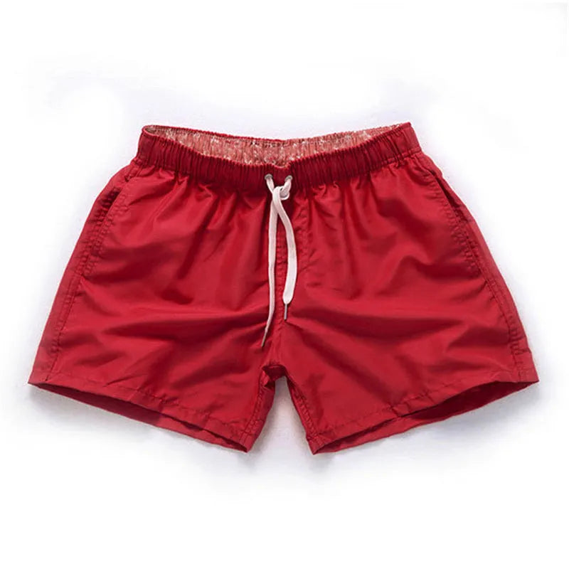 Man wearing straight-leg polyester beach shorts in a bright colour on the sand.