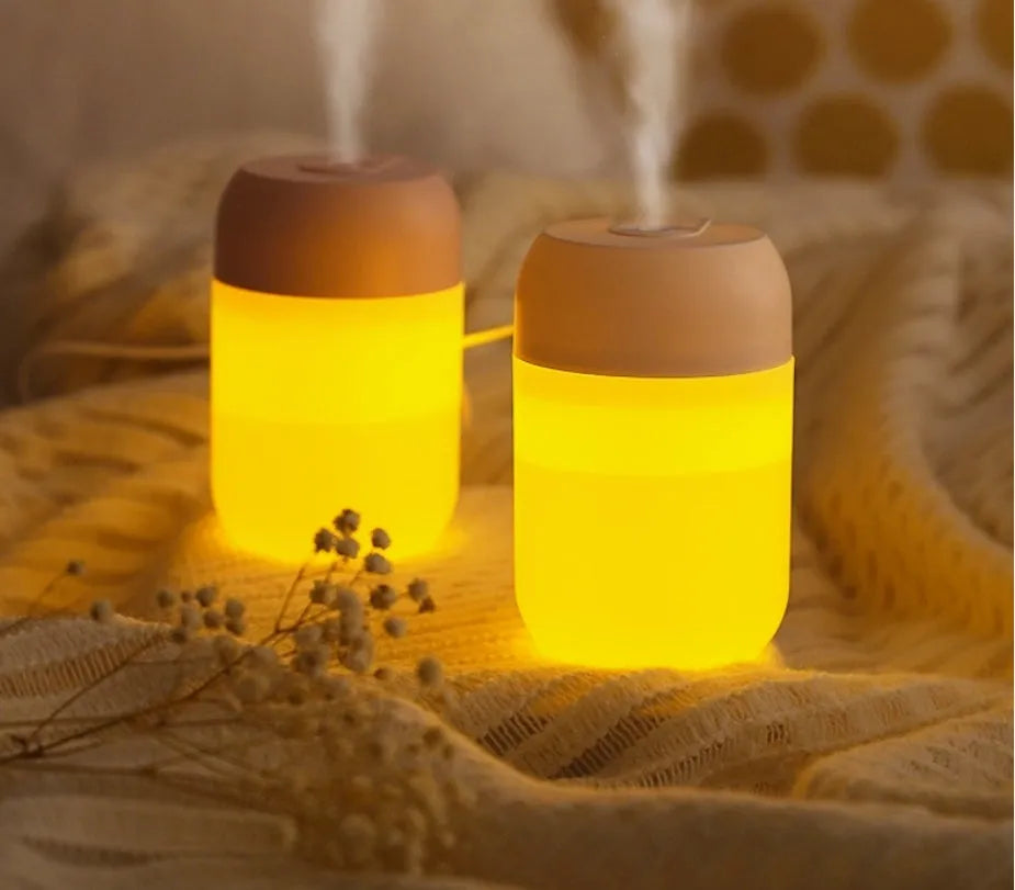 White cylindrical humidifier with USB cable on a desk, showing compact 15cm height and aromatherapy function for essential oils.