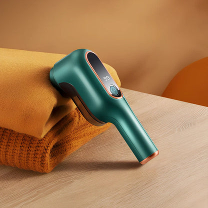 Rechargeable green lint trimmer removing fabric balls from wool jumper, digital display showing speed, 15 cm size with spare blades