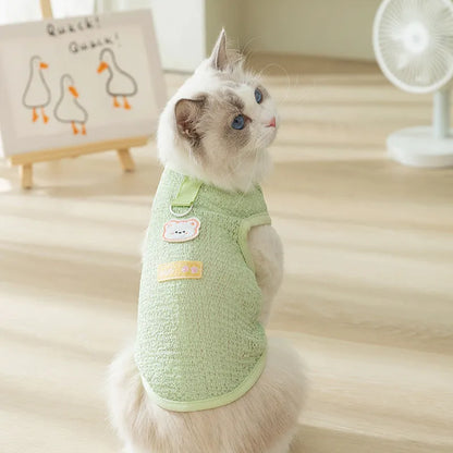 Green knitted cat clothing with a cartoon bear patch, showing hollowed-out breathable design.