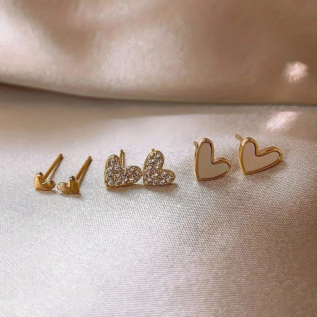 Three pairs of heart-shaped electroplated earrings in gold, black, black and white, and pink colours