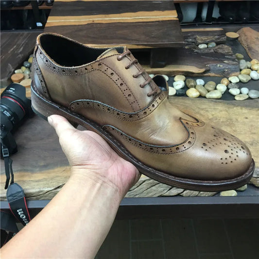 Men's light brown vintage engraved leather shoes with distressed detailing, round toe, and lace-up closure on wooden surface